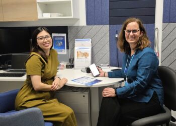 (From left) Raisse Tjoa and Kate Rutledge in the Innovation Centre, displaying the Hearing WB app and related flyer. Image: Hearing Australia.